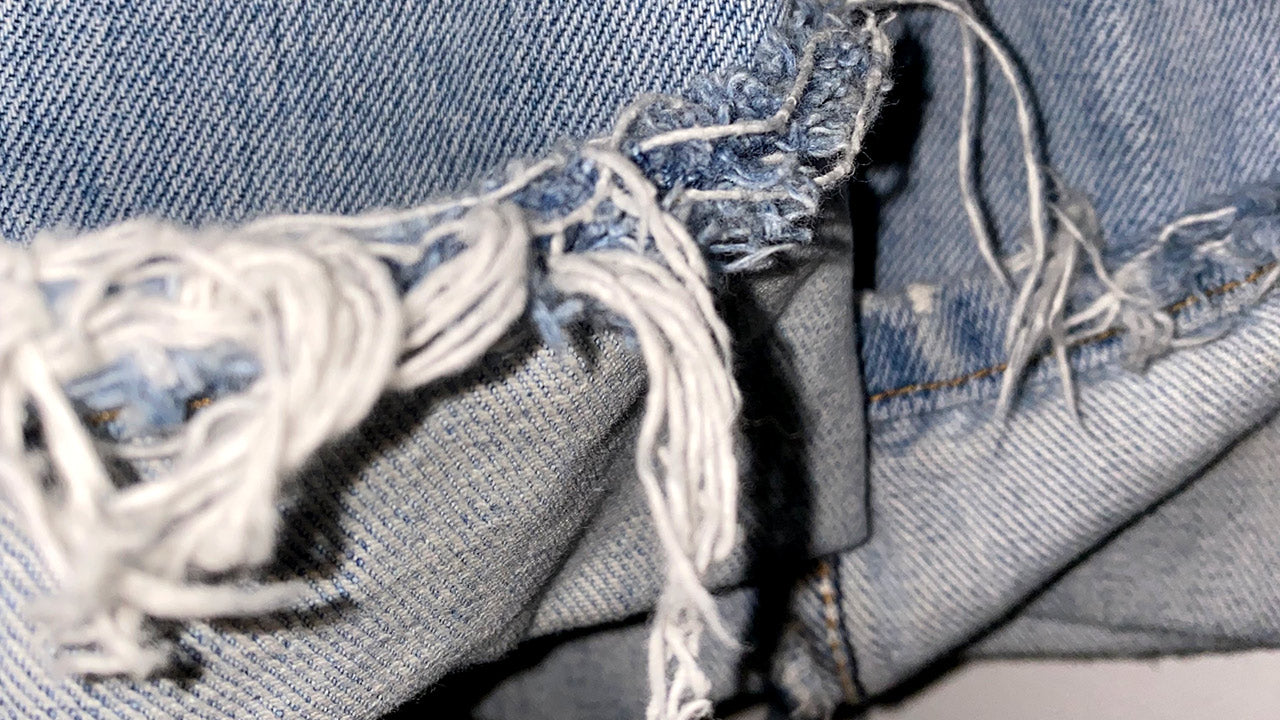 Denim jeans fraying loose threads at the hem.